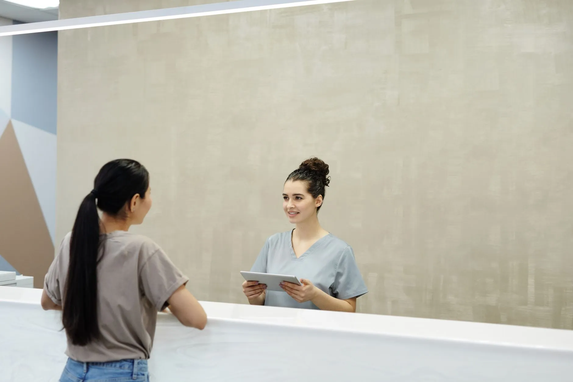 A receptionist smiling at a patient across a medical reception desk.