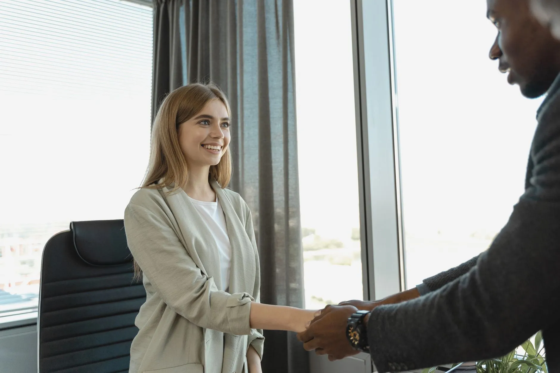 Two people shaking hands across a desk in an office.