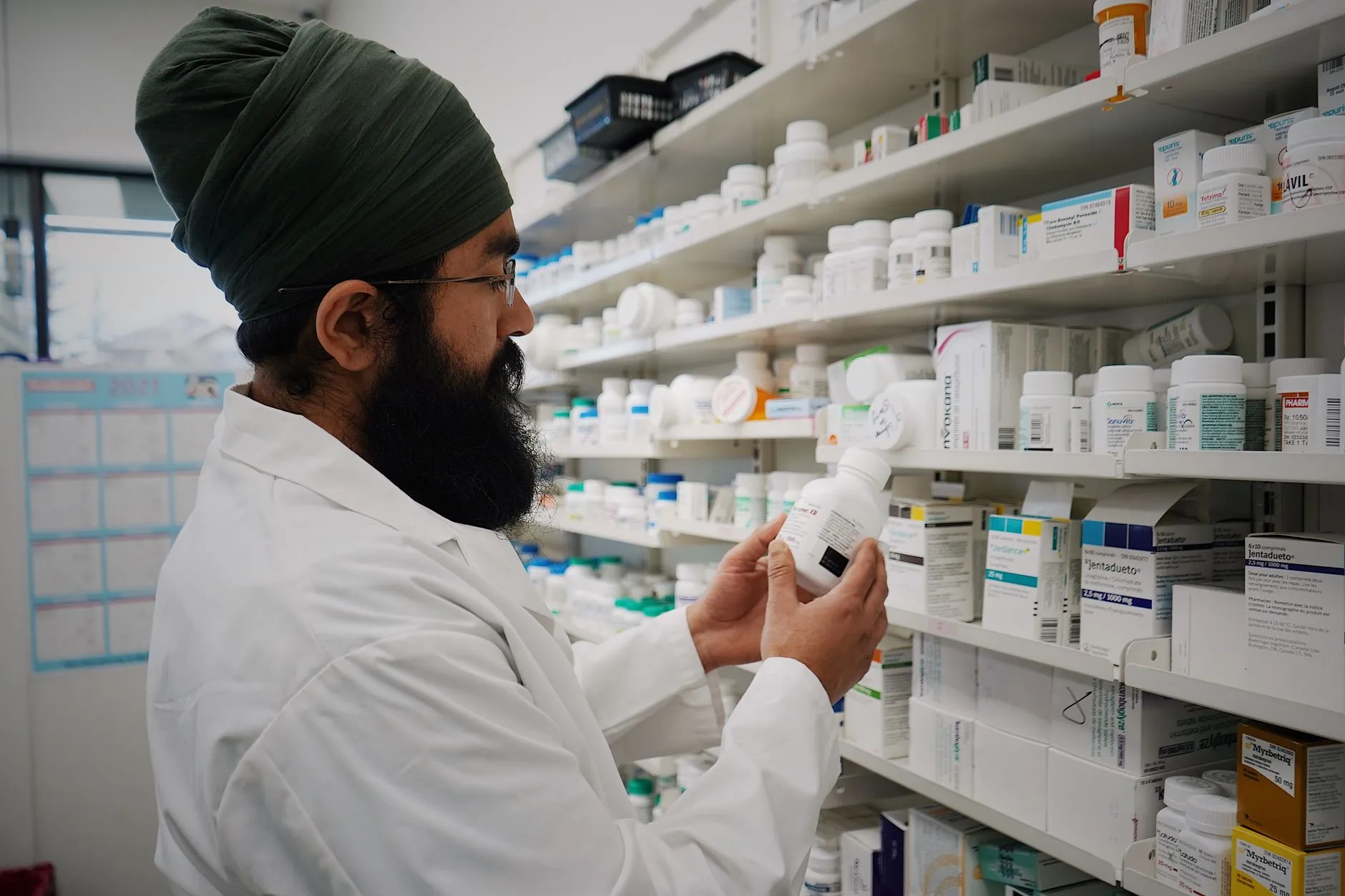 A pharmacist organising medicines on the shelves behind a counter.