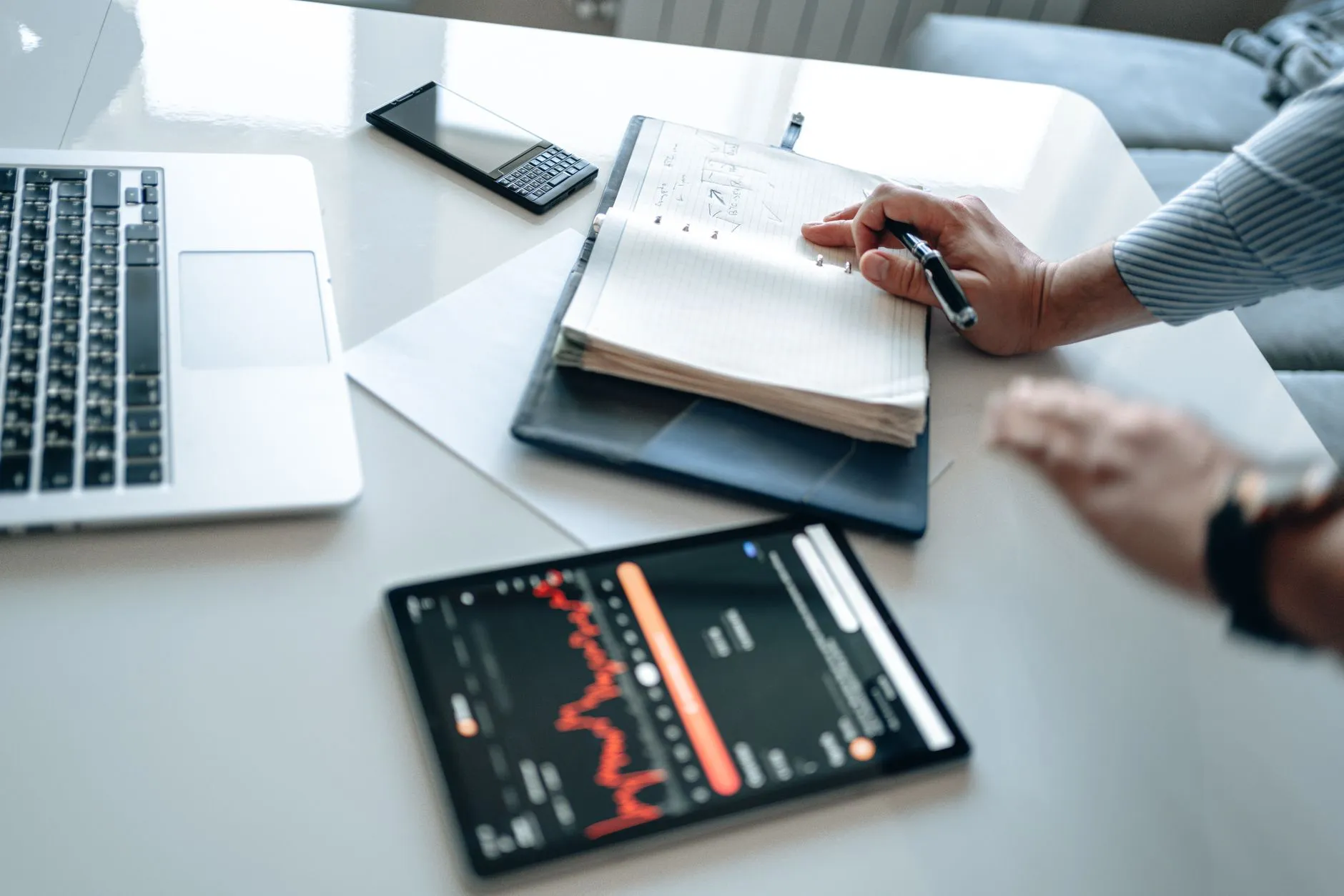 A notebook, tablet and laptop open side by side on a desk.