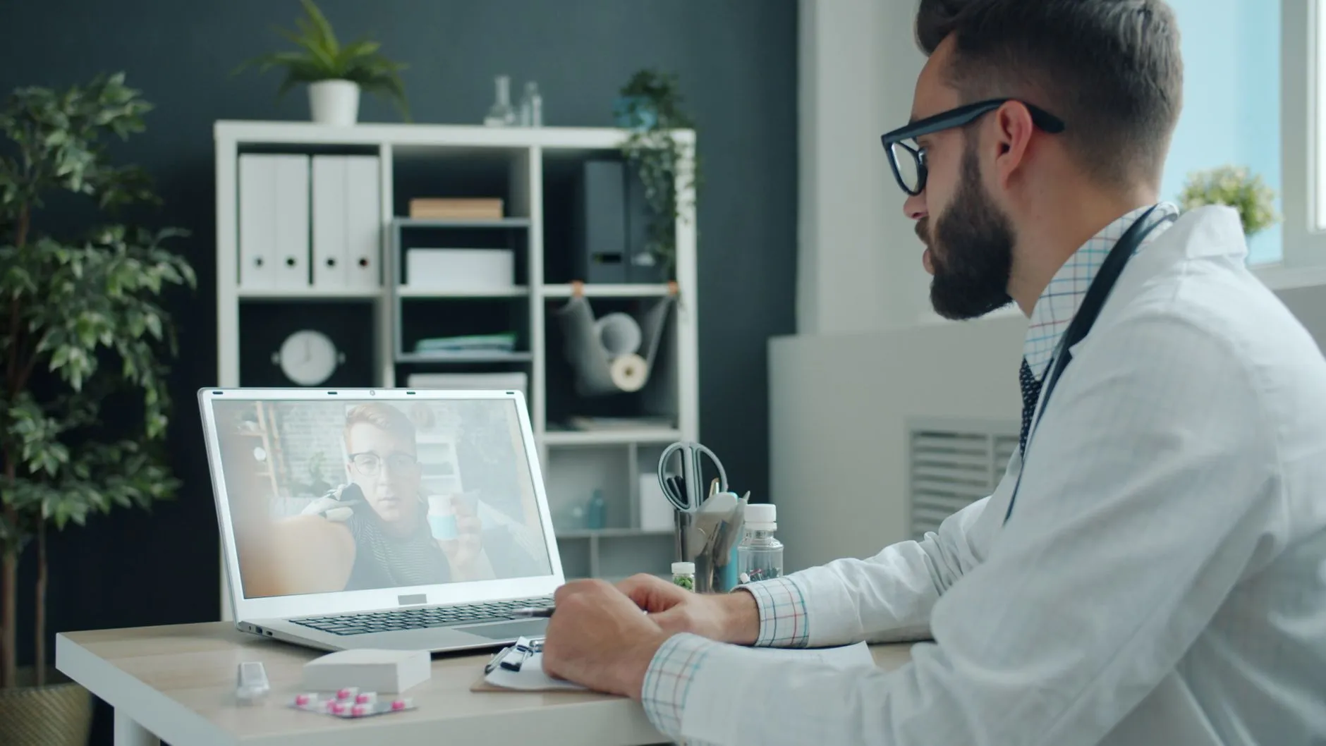 A doctor consulting a patient over a video call on a laptop.